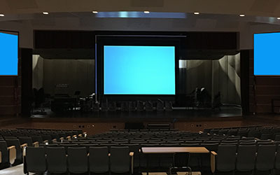 Three large screens inside a dark auditorium