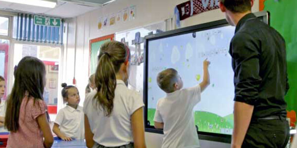 Kids in a classroom playing with a large touchscreen display from Data Projections