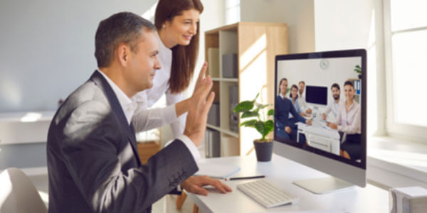 Data Projections specialists waving on a conference call to a full boardroom of clients