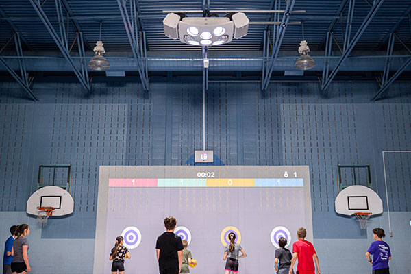 Children lining up to play with a 3D camera projector in a gym