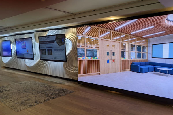 Three large monitors next to a wall digital display in a long hallway