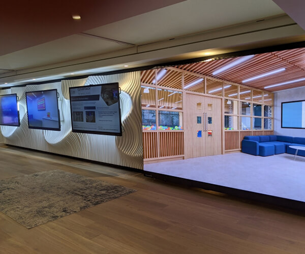 Three large monitors next to a wall digital display in a long hallway