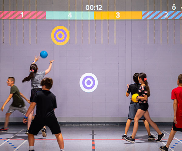 Children playing wall ball using a 3D camera projectors in a gym